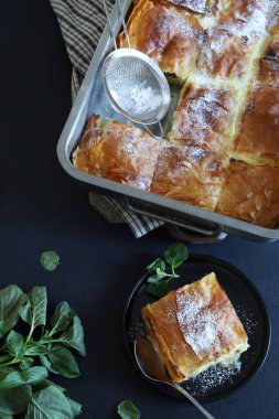 Yunan mutfağı. Ev yapımı geleneksel Yunan Bougatsa peynirle doldurulmuş ve üzerine pudra şekeri serpiştirilmiş fillo hamur işi. Tam üstte.
