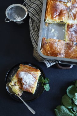 Yunan mutfağı. Ev yapımı geleneksel Yunan Bougatsa 'sı, peynirle doldurulmuş fillo hamur işi ve üzerine şeker serpiştirilmiş. Tam üstte.