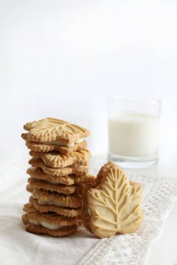 Klasik Kanada akçaağaç yaprağı şekilli kurabiyeler. İki çıtır kurabiyeyle beyaz arka planda bir bardak süt arasına sıkıştırılmış akçaağaç kreması. Boşluğu kopyala.