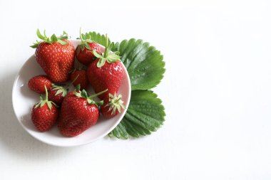 Beyaz arka planda izole edilmiş bir tabakta taze çilek grubu. Sağlıklı ve vejetaryen yemekleri. Tam üstte.