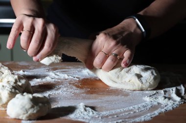 Un kaplı bir masada hamur mayasıyla çalışan elleri olan kadın. Koyu arkaplan. 