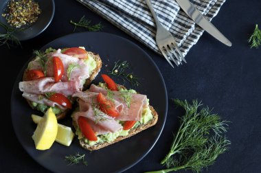 Fırında jambonlu avokado tostu (prosciutto) ve siyah arka planda domates. Sağlıklı gıda konsepti. Genel Görünüm.