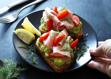Fırında jambonlu avokado tostu (prosciutto) ve siyah arka planda domates. Sağlıklı gıda konsepti. Genel Görünüm.