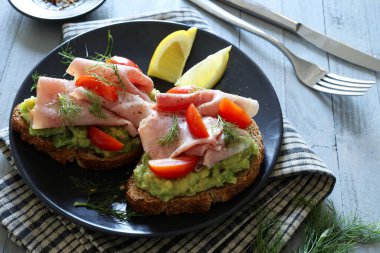 Fırında jambonlu avokado tostu (prosciutto) ve siyah arka planda domates. Sağlıklı gıda konsepti. Genel Görünüm.