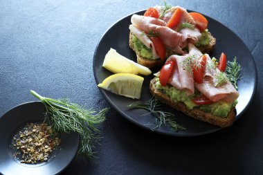 Fırında jambonlu avokado tostu (prosciutto) ve siyah arka planda domates. Sağlıklı gıda konsepti. Genel Görünüm.