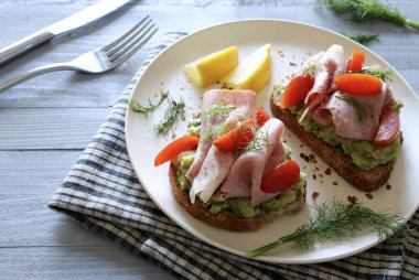 Fırında jambonlu avokado tostu (prosciutto) ve gri arka planda domates. Sağlıklı gıda konsepti. Genel Görünüm.