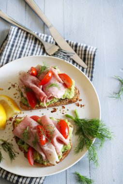 Fırında jambonlu avokado tostu (prosciutto) ve gri arka planda domates. Sağlıklı gıda konsepti. Genel Görünüm.