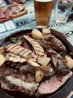 Pirzola, sosis, sığır eti, tavuk ve fırında patates ile nefis ızgara tabağı. Tam üstte.