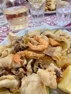 Kızarmış karides, kalamar ve sebzeli lezzetli bir yemek ve İtalyan restoranında arka planda bir bardak beyaz şarap. Tam üstte.