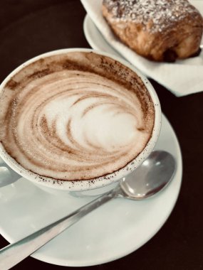 Bir fincan kapuçino ve İtalyan restoranında lezzetli bir kruvasan. Kahvaltı konsepti. Tam üstte.