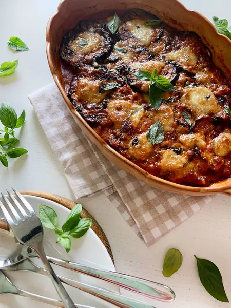 stock image Baked aubergine parmigiana. Dish based on aubergines, tomato puree, basil, garlic and cheese. Fresh basil leaves decoration. Italian food. Directly above.