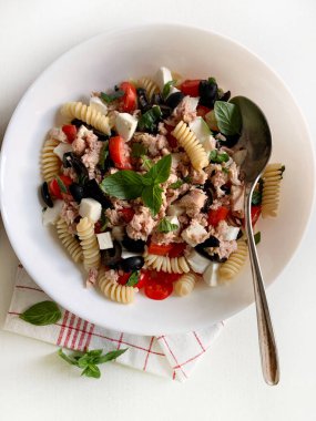 İtalyan yemeği. Ton balıklı makarna salatası, kiraz domatesleri, mozzarella ve beyaz tabakta fesleğen yapraklarıyla süslenmiş zeytinler. Sağlıklı yaz yemekleri. Tam üstte.