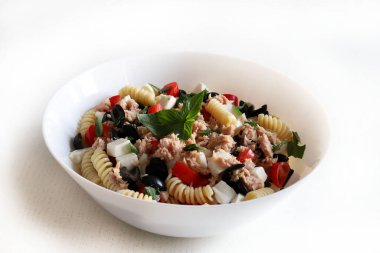 Italian food. Pasta salad with tuna, cherry tomatoes, mozzarella and olives decorated with basil leaves on white plate. Healthy  summer food. Directly above.