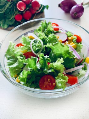 Sebzeli taze salata. Beyaz arka planda cam bir kasede kıvırcık salata, salatalık, domates, soğan, mısır ve turp. Diyet beslenme. Boşluğu kopyala.