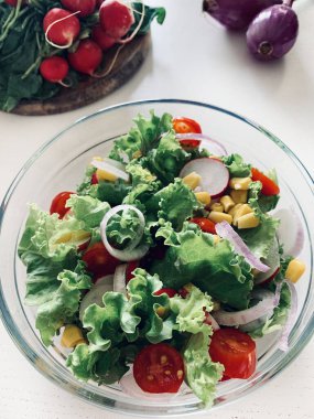 Sebzeli taze salata. Beyaz arka planda cam bir kasede kıvırcık salata, salatalık, domates, soğan, mısır ve turp. Diyet beslenme. Boşluğu kopyala.
