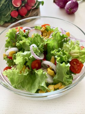 Sebzeli taze salata. Beyaz arka planda cam bir kasede kıvırcık salata, salatalık, domates, soğan, mısır ve turp. Diyet beslenme. Boşluğu kopyala.
