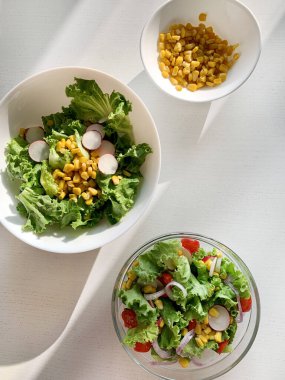 Sebzeli taze salata. Beyaz arka planda kıvırcık salata, salatalık, domates, soğan, mısır ve turp. Diyet beslenme. Uzayı kopyala Tam üstte.