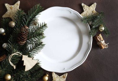 Noel ağacı dalı, boş beyaz tabak, arka planda Noel süsü. Tam üstte. Boşluğu kopyala.