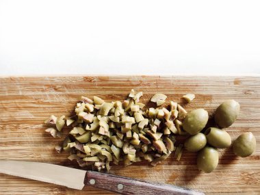 Doğranmış yeşil zeytin ve bıçak beyaz ahşap arka planda izole edilmiş tahta kesim tahtasının üzerinde. Tam üstte. Vejetaryen yemeği..