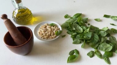 Taze organik fesleğen yaprakları çam fıstığı, zeytin yağı ve pesto sosu yapmak için ahşap havan topunun yanındaki beyaz ahşap masaya düşer. Yemek pişirmek için baharatlar. Sağlıklı bir yaşam tarzı. İtalyan yemeği. Yavaş çekim videosu.