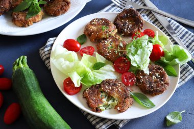 Ev yapımı vejetaryen kabak köftesi ve gri arka planda karışık sebze salatası. Sağlıklı ve vejetaryen yemekleri. Tam üstte.