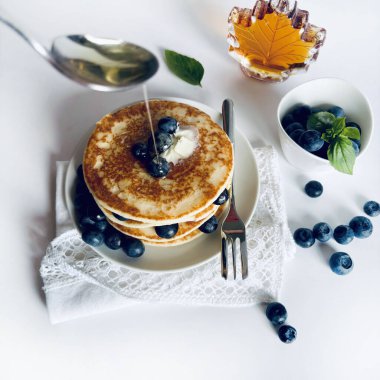 Beyaz bir zemin üzerinde akçaağaç şurubu, tereyağı ve yaban mersinli lezzetli krep yığını. Lezzetli ev yapımı kahvaltı ya da öğle yemeği. 