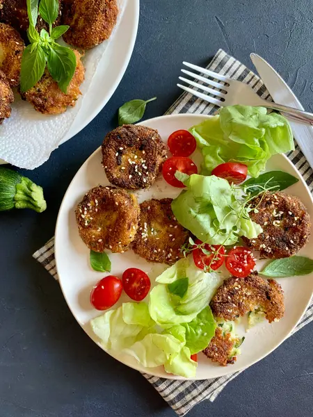Ev yapımı vejetaryen kabak köftesi ve gri arka planda karışık sebze salatası. Sağlıklı ve vejetaryen yemekleri. Tam üstte.