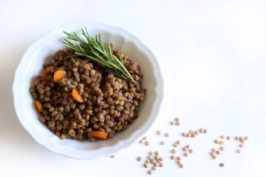 Beyaz bir masada, otlarla tatlandırılmış ev yapımı mercimek ve çiğ mercimek. Sağlıklı ve vejetaryen yemekleri. Tam üstte.