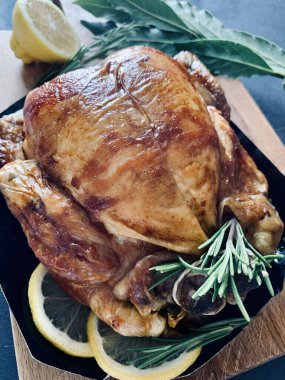 Lezzetli kavrulmuş tavuk taze bitkilerle süslenmiş ve siyah masada limon dilimleri var. Tam üstte.