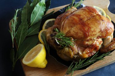 Lezzetli kavrulmuş tavuk taze bitkilerle süslenmiş ve siyah masada limon dilimleri var. Tam üstte.