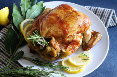 Lezzetli kavrulmuş tavuk taze bitkilerle süslenmiş ve siyah masada limon dilimleri var. Tam üstte.