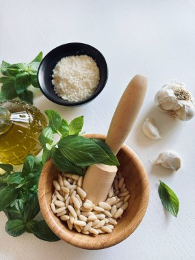 Yeşil fesleğen, sarımsak, çam fıstığı, parmesan peyniri, beyaz ahşap bir masada zeytin yağı gibi ev yapımı pesto sosu yapmak için taze sağlıklı malzemeler. Tam üstte. İtalyan yemeği..