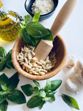 Yeşil fesleğen, sarımsak, çam fıstığı, parmesan peyniri, beyaz ahşap bir masada zeytin yağı gibi ev yapımı pesto sosu yapmak için taze sağlıklı malzemeler. Tam üstte. İtalyan yemeği..