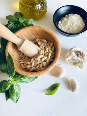 Yeşil fesleğen, sarımsak, çam fıstığı, parmesan peyniri, beyaz ahşap bir masada zeytin yağı gibi ev yapımı pesto sosu yapmak için taze sağlıklı malzemeler. Tam üstte. İtalyan yemeği..