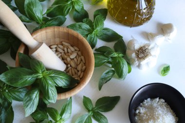 Yeşil fesleğen, sarımsak, çam fıstığı, parmesan peyniri, beyaz ahşap bir masada zeytin yağı gibi ev yapımı pesto sosu yapmak için taze sağlıklı malzemeler. Tam üstte. İtalyan yemeği..