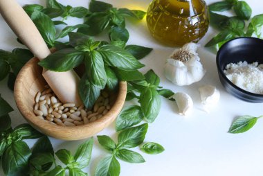 Yeşil fesleğen, sarımsak, çam fıstığı, parmesan peyniri, beyaz ahşap bir masada zeytin yağı gibi ev yapımı pesto sosu yapmak için taze sağlıklı malzemeler. Tam üstte. İtalyan yemeği..