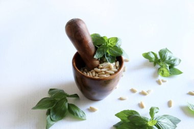 Çam fıstıklı ahşap havan ve beyaz ahşap arka planda taze fesleğen yaprakları. Tam üstte.