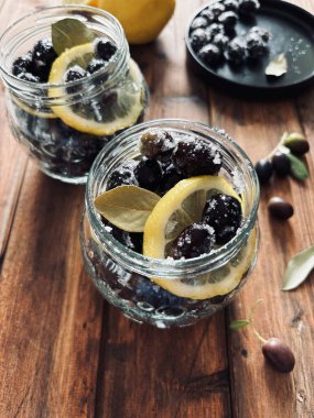 Suda terbiye edilmiş siyah zeytinler, ahşap arka planda kavanozlarda tuz ve limon. Tam üstte.