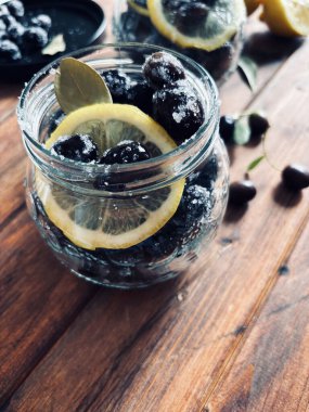 Suda terbiye edilmiş siyah zeytinler, ahşap arka planda kavanozlarda tuz ve limon. Tam üstte.