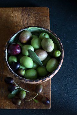 Koyu arka planda izole edilmiş ahşap kesim tahtasındaki taze zeytinler. Vejetaryen ve sağlıklı yiyecekler. Tam üstte.