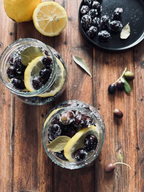 Suda marine edilmiş siyah taze zeytinler, ahşap arka planda izole edilmiş kavanozlarda tuz ve limon. Tam üstte