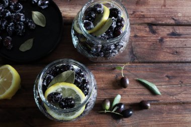 Suda marine edilmiş siyah taze zeytinler, ahşap arka planda izole edilmiş kavanozlarda tuz ve limon. Tam üstte