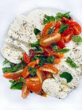 Klasik İtalyan caprese salatası dilimlenmiş mozzarella, domates, fesleğen yaprağı ve beyaz tabakta zeytinyağı. Yaz yemeği. İtalyan gıda konsepti. 