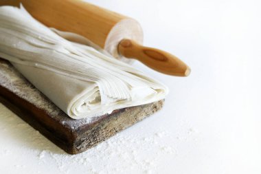 Unlu ahşap kesme tahtasının üzerinde taze fillo hamuru ve beyaz ahşap bir masada izole edilmiş merdane. Boşluğu kopyala.