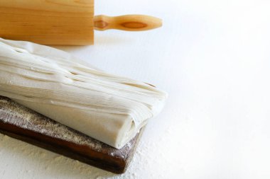 Unlu ahşap kesme tahtasının üzerinde taze fillo hamuru ve beyaz ahşap bir masada izole edilmiş merdane. Boşluğu kopyala.