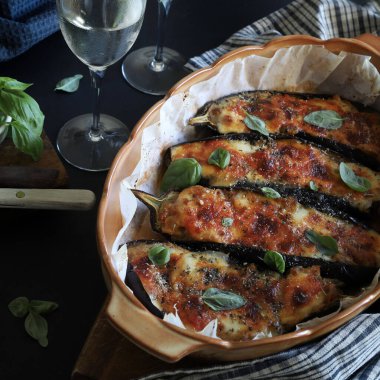 Mozarella peynirli ev yapımı fırında patlıcan, doğranmış domates ve koyu arkaplanda taze fesleğen yaprakları. Vejetaryen yemeği. Tam üstte.