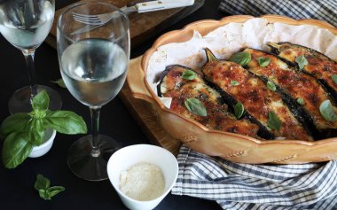 Mozarella peynirli ev yapımı fırında patlıcan, doğranmış domates ve koyu arkaplanda taze fesleğen yaprakları. Vejetaryen yemeği. Tam üstte.