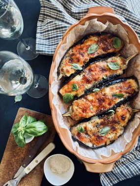 Mozarella peynirli ev yapımı fırında patlıcan, doğranmış domates ve koyu arkaplanda taze fesleğen yaprakları. Vejetaryen yemeği. Tam üstte.