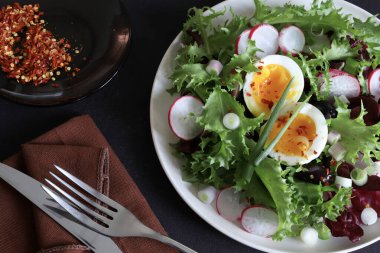 Beyaz tabakta servis edilen haşlanmış yumurtalarla birlikte taze sağlıklı sebze salatası, koyu arkaplan. Tam üstte.