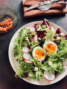 Beyaz tabakta servis edilen haşlanmış yumurtalarla birlikte taze sağlıklı sebze salatası, koyu arkaplan. Tam üstte.